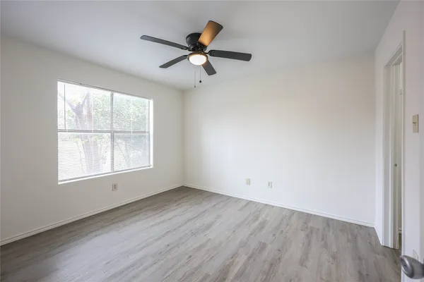 an empty room with wooden floor fan and windows