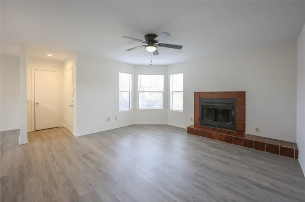 an empty room with wooden floor a ceiling fan a fireplace and windows