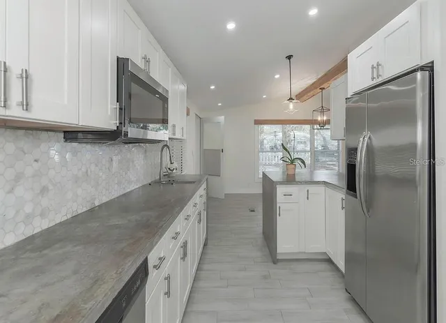 a kitchen with stainless steel appliances granite countertop a refrigerator a sink and white cabinets