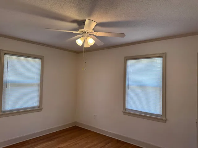 an empty room with wooden floor fan and windows