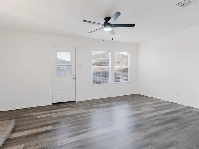 an empty room with wooden floor chandelier fan and windows