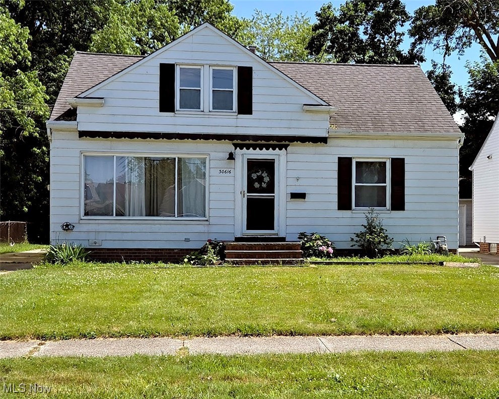 Bungalow with roof with shingles, entry steps, and a front lawn