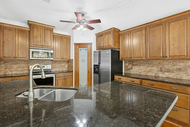 a kitchen with granite countertop a refrigerator a sink a stove and cabinets