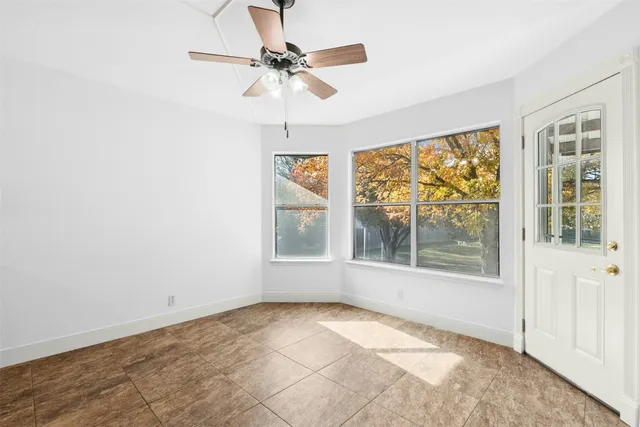 an empty room with chandelier fan and windows