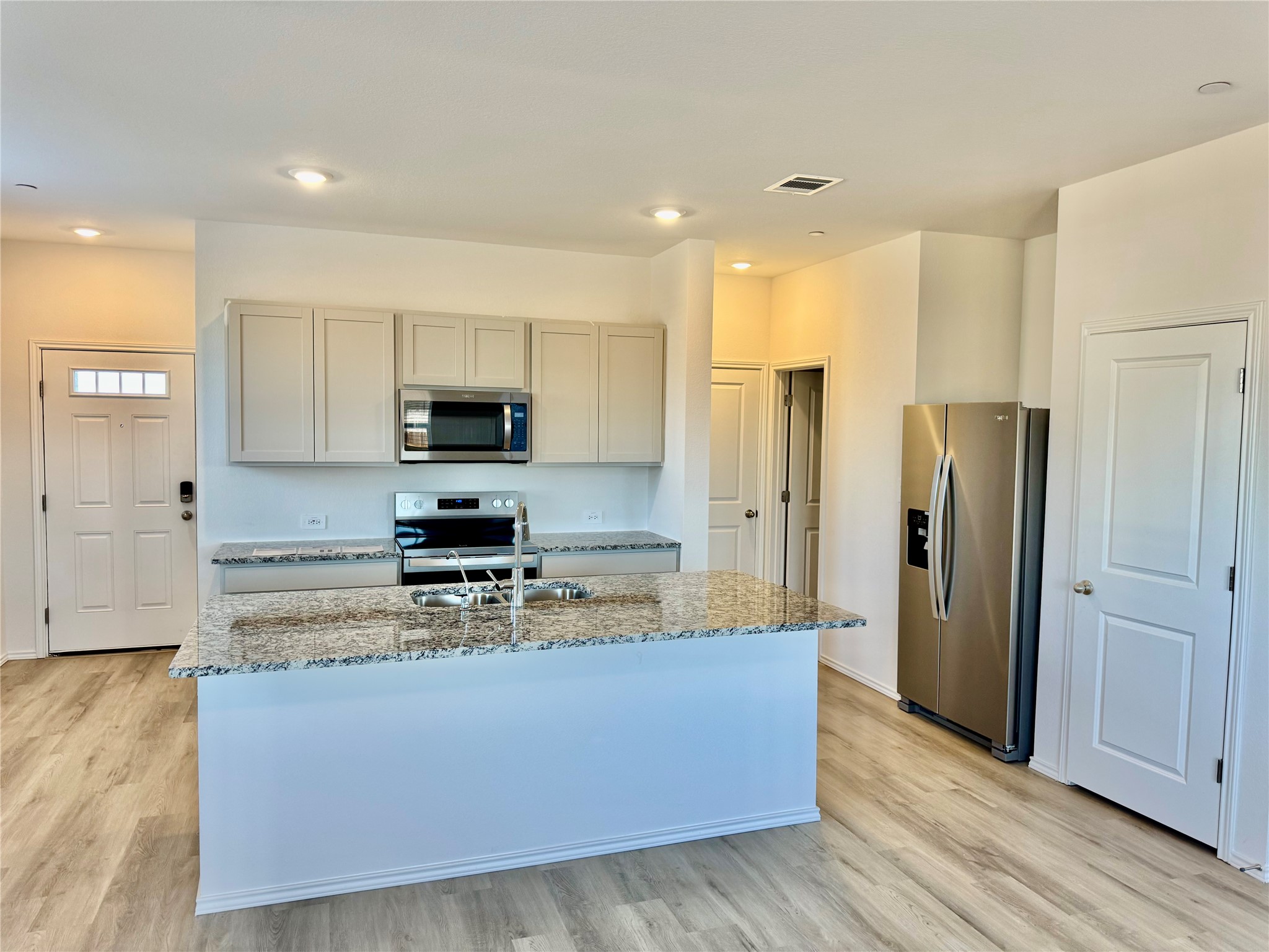 104 Calcite Road, Unit 1 Kyle, TX 78640 - Photo 2 of 7 Kitchen featuring appliances with stainless steel finishes, light stone counters, light wood-style flooring, and a kitchen island with sink