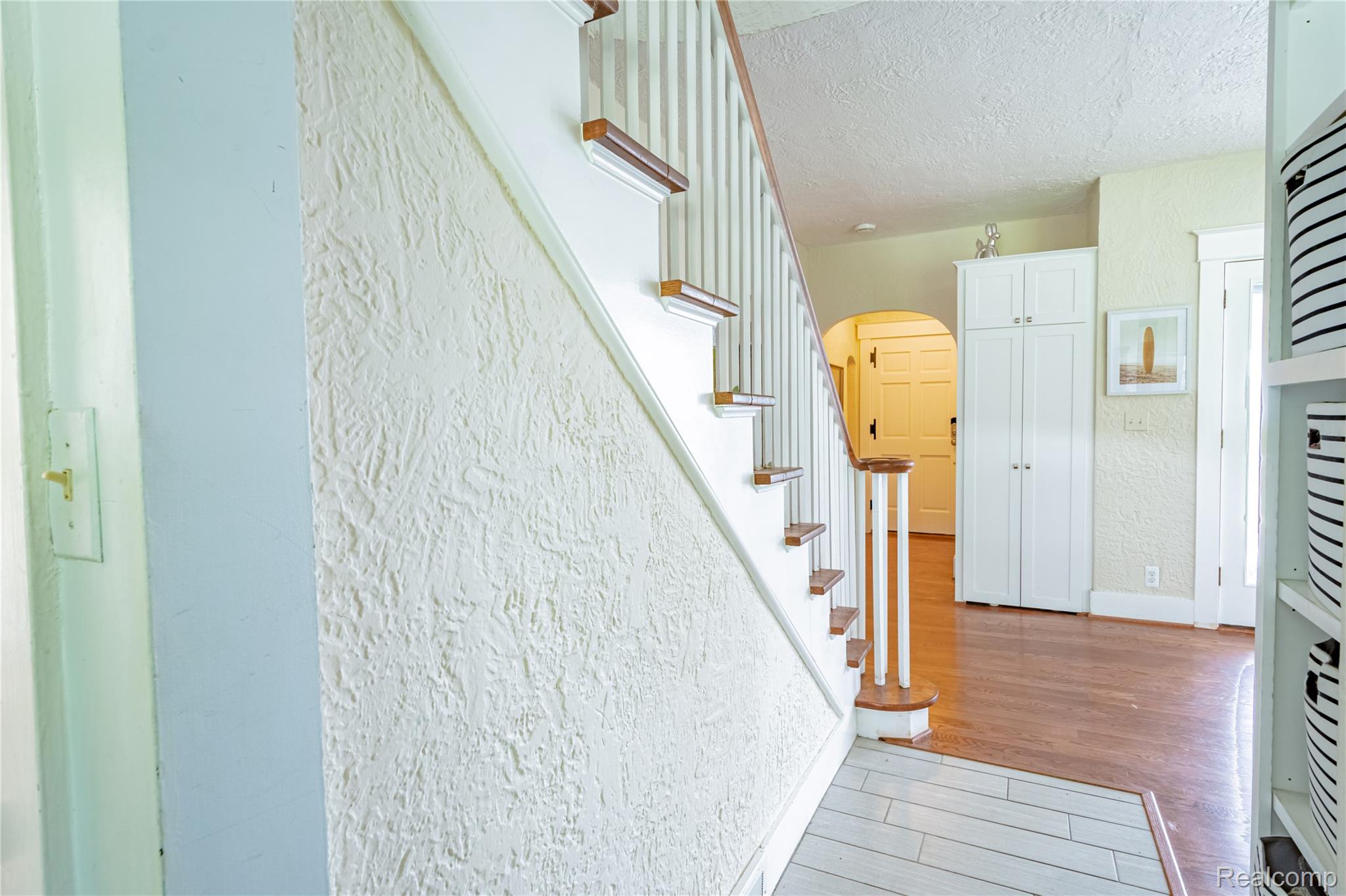 5630 Lakeshore Road Fort Gratiot, MI 48059 - Photo 10 of 49 Hardwood flooring extending from an arched entryway, complemented by a white wood staircase with wood-finish treads and balusters