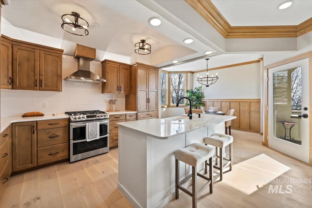 79 East Aikens Road, Unit 202 Eagle, ID 83616 - Photo 12 of 47 Kitchen featuring double oven range, ornamental molding, brown cabinetry, wall chimney range hood, and a breakfast bar