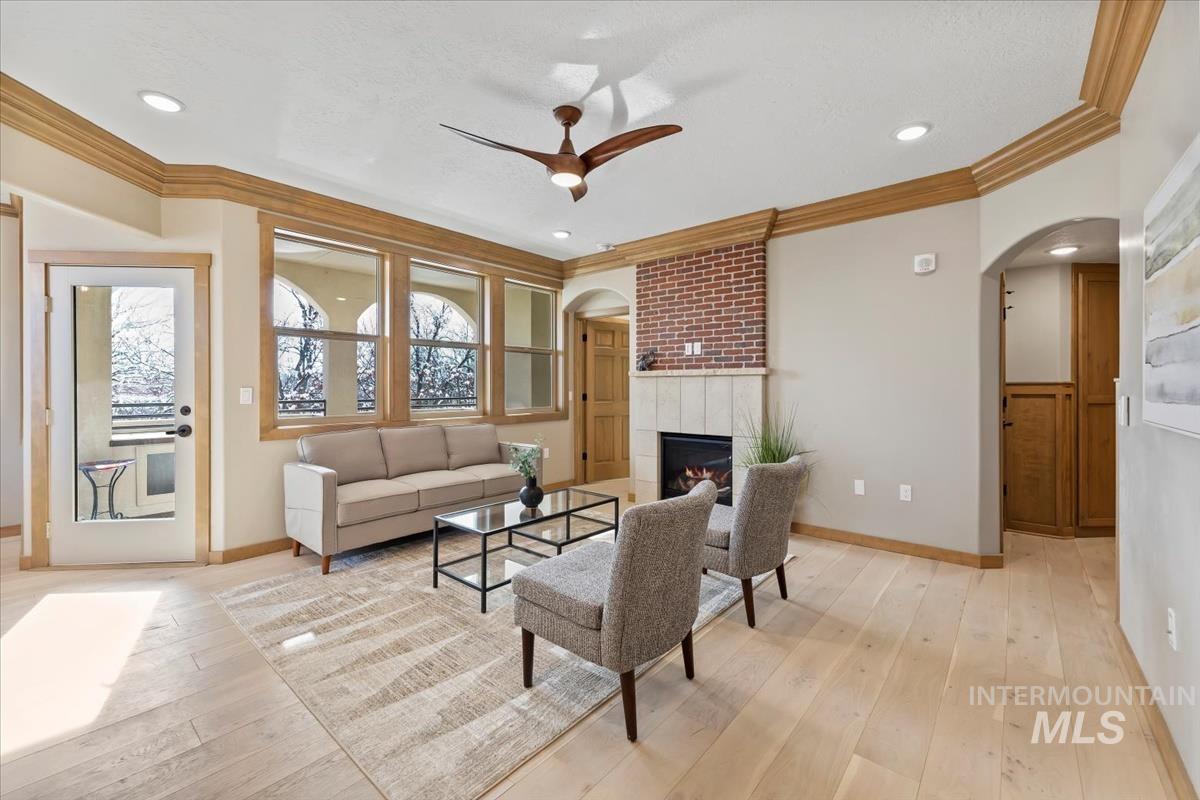 79 East Aikens Road, Unit 202 Eagle, ID 83616 - Photo 5 of 47 Living room featuring arched walkways, ceiling fan, crown molding, light wood-style floors, and a tiled fireplace