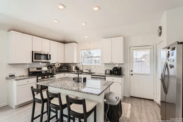 a kitchen with stainless steel appliances granite countertop a stove top oven a refrigerator a sink and white cabinets with wooden floor