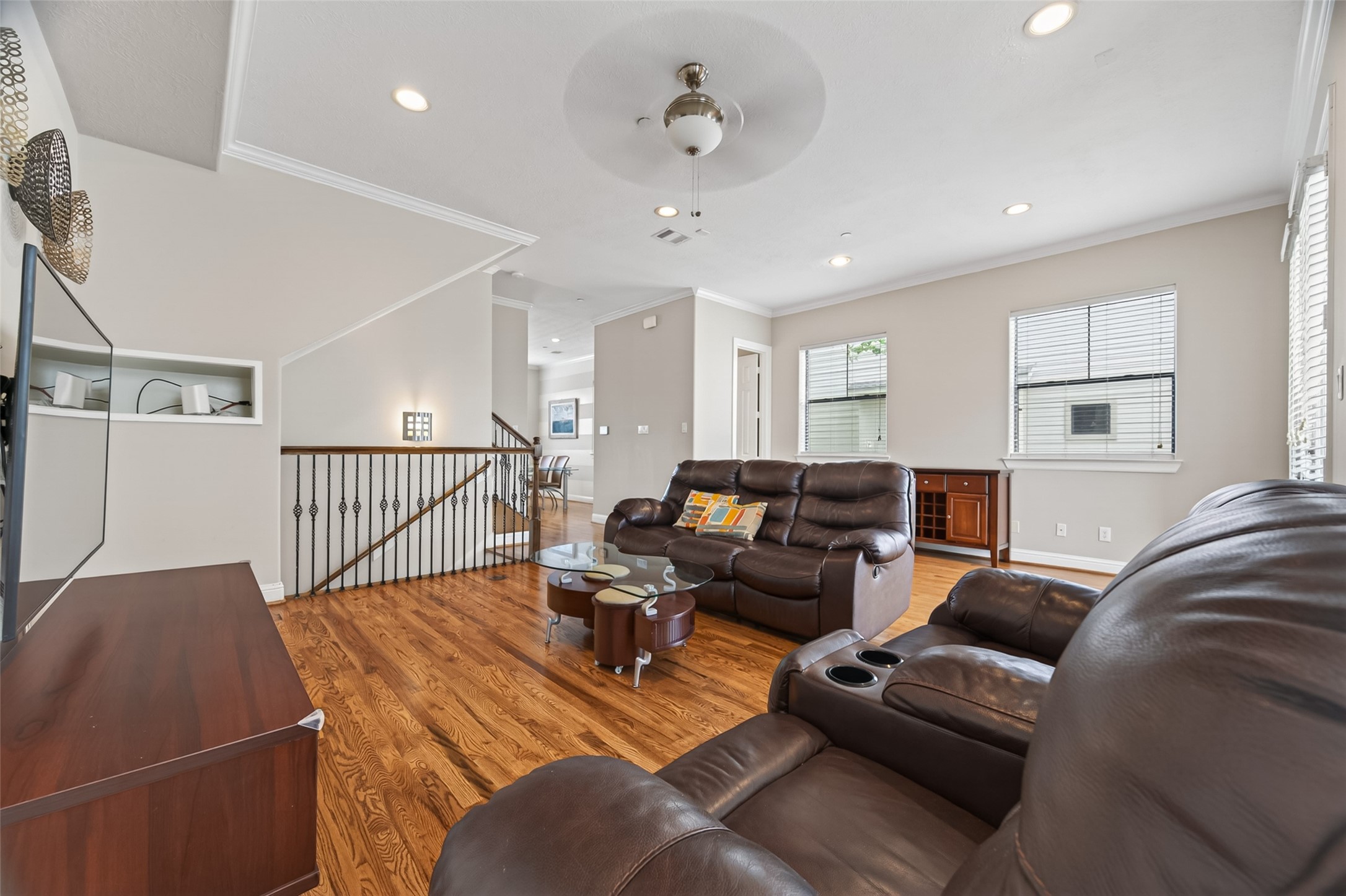 2611 Riverside Drive, Unit C Houston, TX 77004 - Photo 25 of 50 This inviting living room features hardwood floors, ample natural light from large windows, and comfortable leather seating. The open layout leads to a dining area, and there's a stylish ceiling fan and modern light fixtures, creating a cozy yet contemporary space.