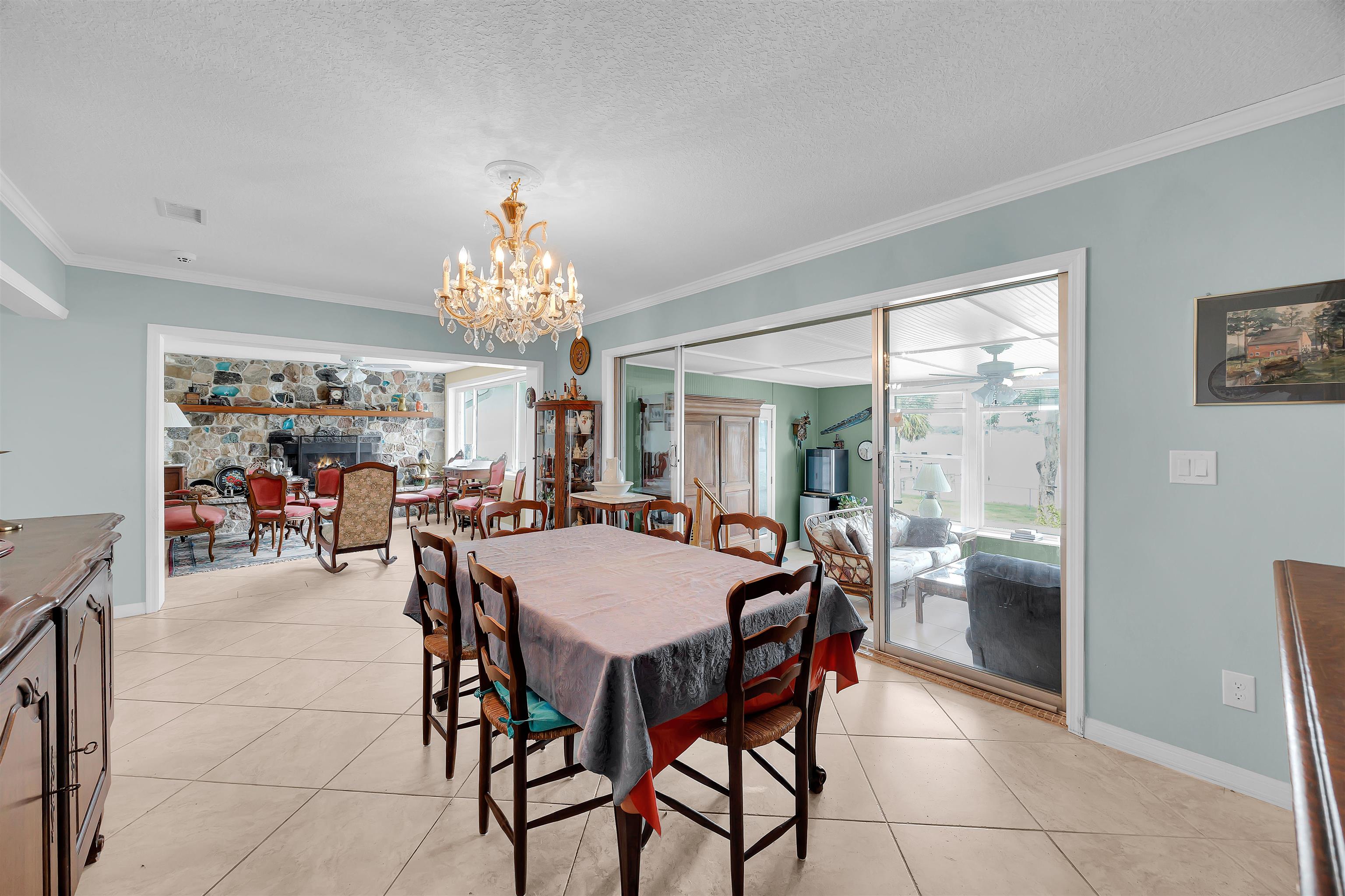 115 Sunset Point Road East Palatka, FL 32131 - Photo 45 of 67 Dining room featuring ornamental molding, a stone fireplace, light tile patterned floors, a textured ceiling, and a chandelier
