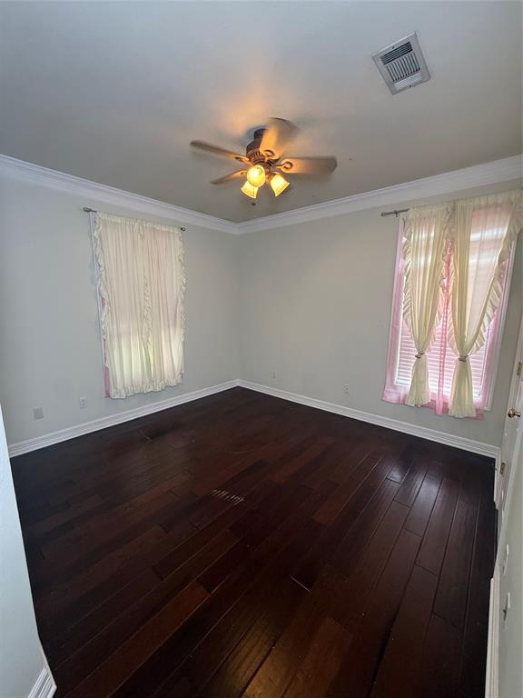 201 Woodhaven Drive Minden, LA 71055 - Photo 16 of 31 Spacious room featuring dark wood-finish flooring, two windows with blinds, a ceiling fan with integrated lighting, a ceiling-mounted air vent, and crown molding
