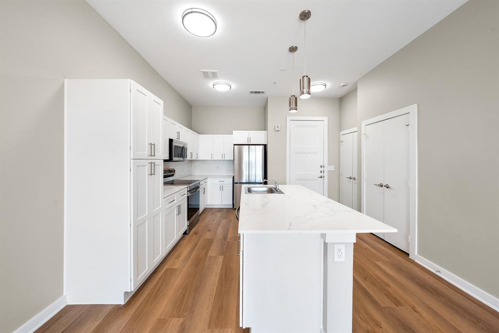 3522 Main Street, Unit 303 Rowlett, TX 75088 - Photo 2 of 23 Kitchen with stainless steel appliances, hanging light fixtures, white cabinetry, a center island with sink, and light wood finished floors
