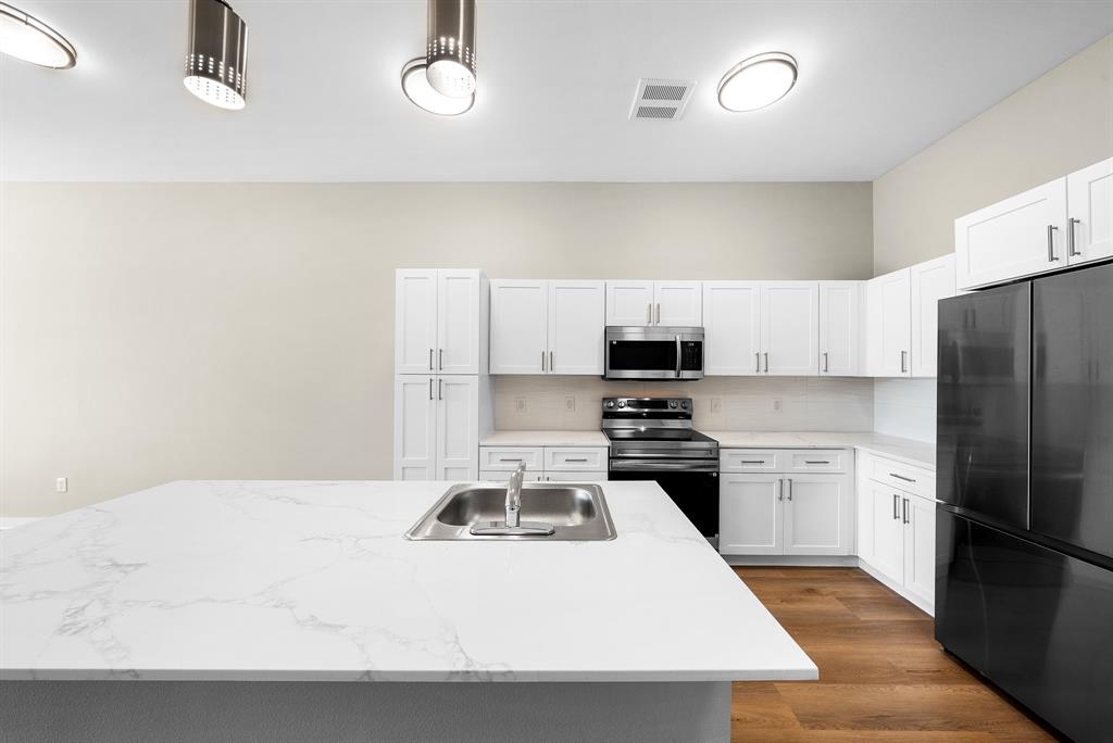 3522 Main Street, Unit 303 Rowlett, TX 75088 - Photo 4 of 23 Kitchen featuring stainless steel appliances, white cabinetry, dark wood-style flooring, backsplash, and an island with sink