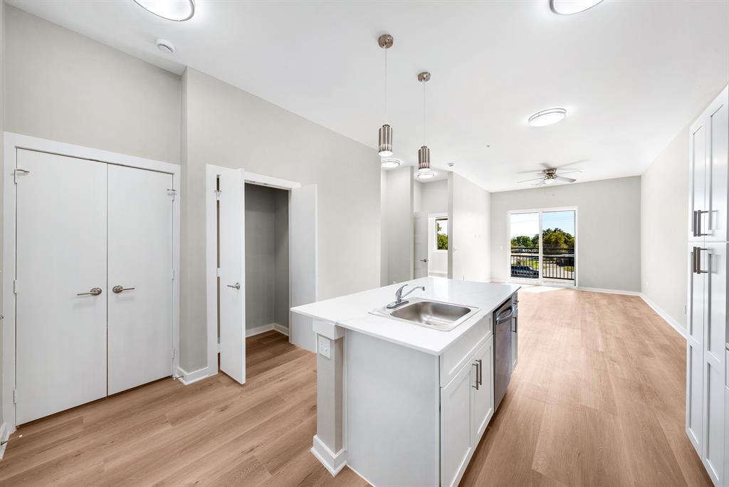 3522 Main Street, Unit 303 Rowlett, TX 75088 - Photo 23 of 23 Kitchen featuring white cabinets, decorative light fixtures, a kitchen island with sink, open floor plan, and light wood-type flooring