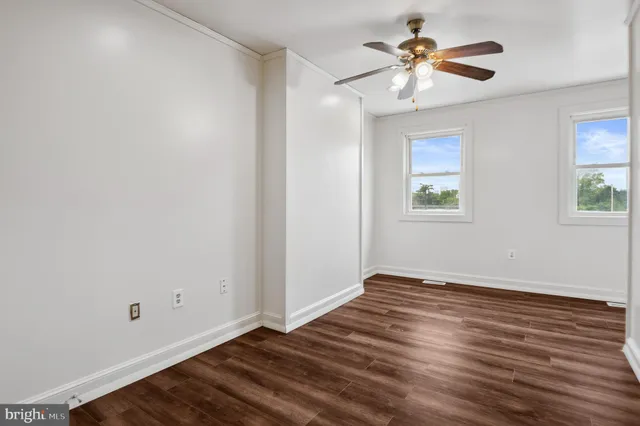 an empty room with wooden floor chandelier fan and windows