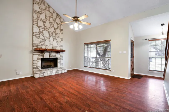 a view of an empty room with wooden floor fireplace and a window