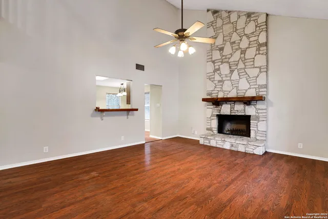 an empty room with wooden floor fireplace chandelier and windows