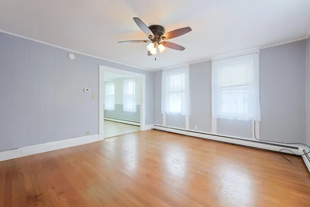an empty room with wooden floor chandelier fan and windows