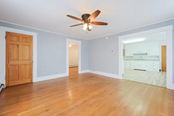 a view of an empty room with wooden floor and a ceiling fan