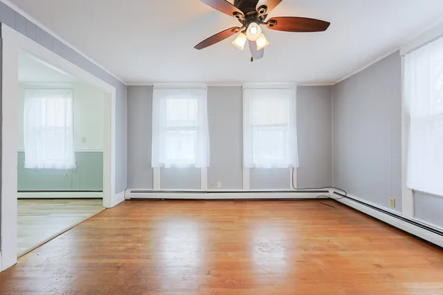 an empty room with wooden floor fan and windows