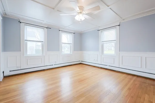 an empty room with wooden floor chandelier fan and windows