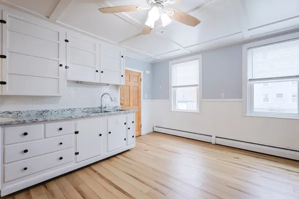 a kitchen with granite countertop a stove a sink and white cabinets with wooden floor