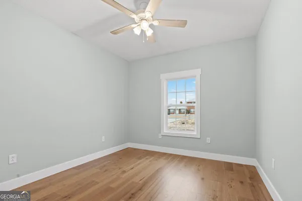 an empty room with wooden floor ceiling fan and windows