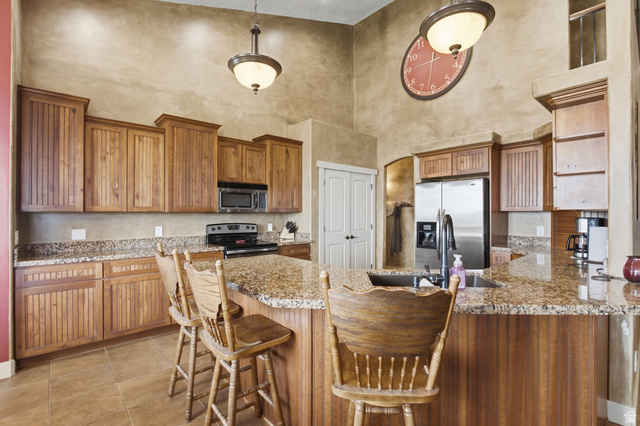 2567 West Rim Rock Drive Stockton, UT 84071 - Photo 10 of 64 Kitchen featuring a center island with bar seating, wood-finish cabinetry, speckled granite countertops, and stainless-steel appliances