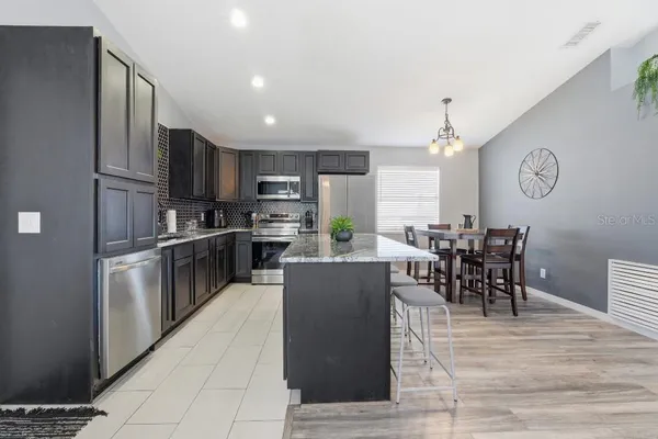 a living room with stainless steel appliances kitchen island granite countertop a table chairs and a refrigerator