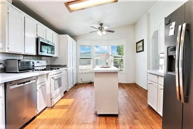 a kitchen with granite countertop a refrigerator a stove top oven a sink dishwasher and white cabinets with wooden floor