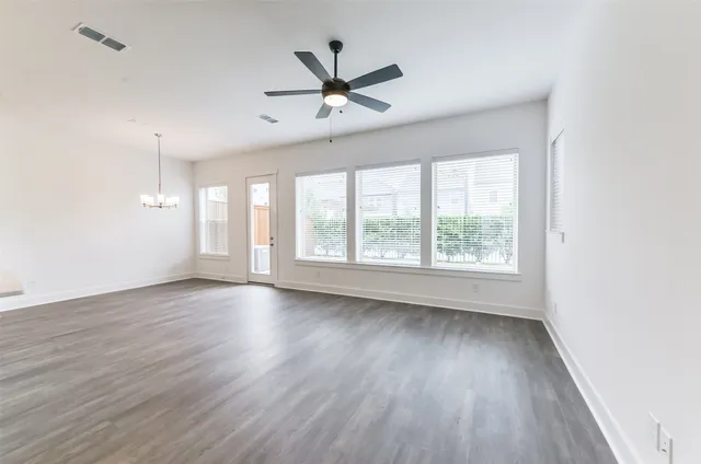 an empty room with wooden floor fan and windows