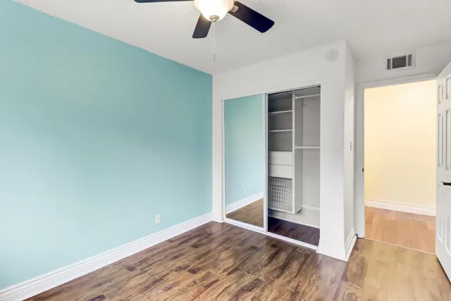 an empty room with wooden floor fan and windows