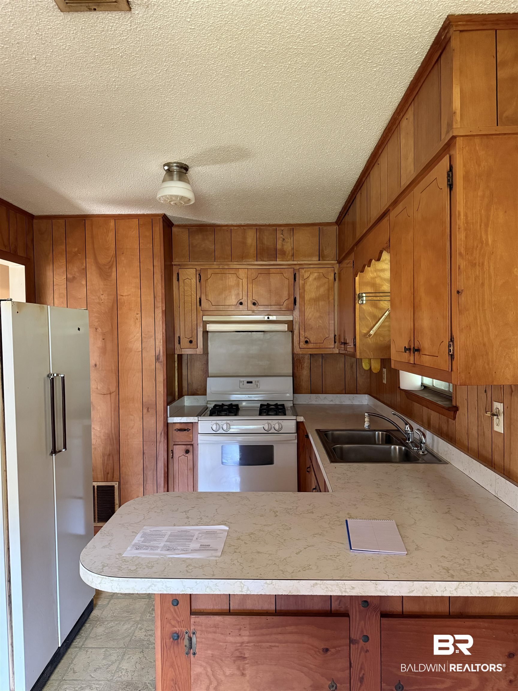 607 West Lee Street Mobile, AL 36611 - Photo 3 of 11 Kitchen with white appliances, wooden walls, light countertops, a textured ceiling, and a peninsula