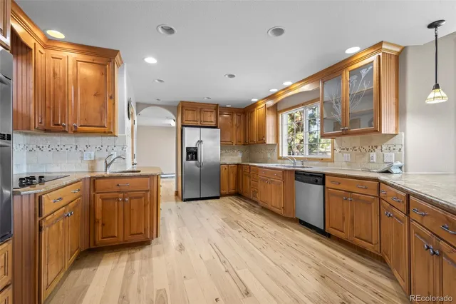 a kitchen with stainless steel appliances granite countertop wooden cabinets a sink and dishwasher a refrigerator with wooden floor