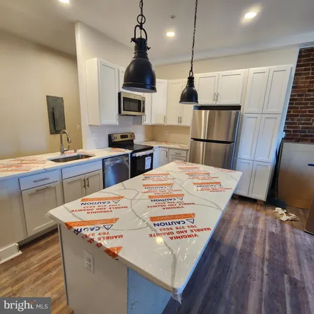 a kitchen with stainless steel appliances kitchen island granite countertop a sink a stove and a wooden floors