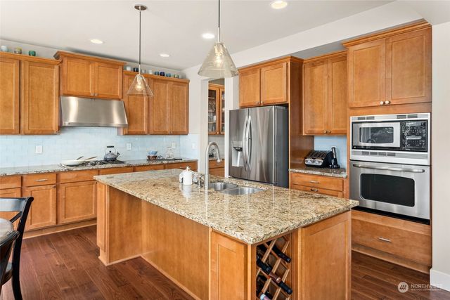 a kitchen with stainless steel appliances granite countertop a kitchen island a stove a refrigerator a sink a dining table and chairs with wooden floor