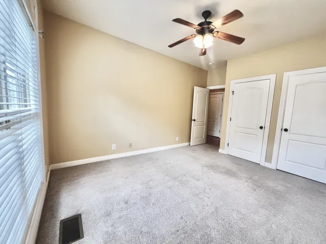 an empty room with chandelier fan and windows