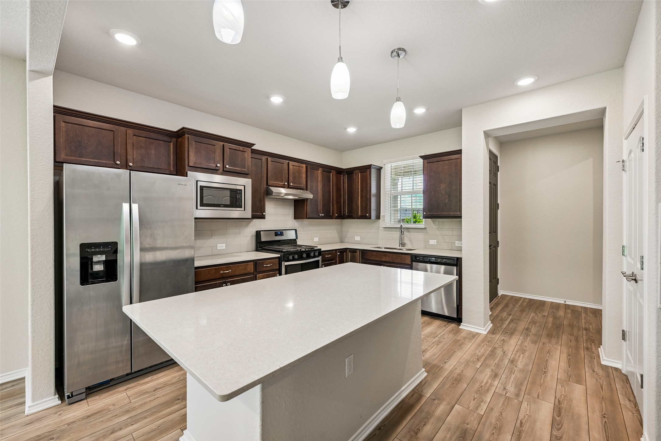 401 Yorktown Street Georgetown, TX 78633 - Photo 10 of 38 Kitchen featuring a central island with a light-toned countertop, wood-finish flooring, dark wood cabinetry, stainless steel appliances, and recessed lighting