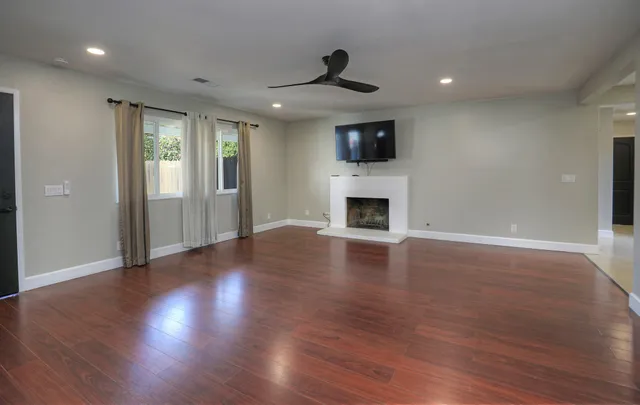 a view of an empty room with wooden floor a fireplace and a window