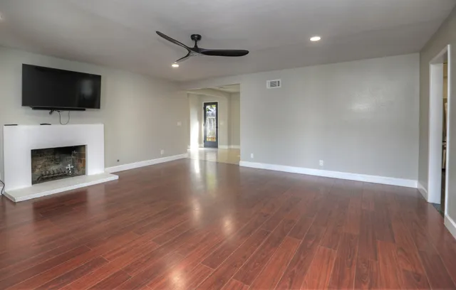 a view of an empty room with wooden floor fireplace and a window