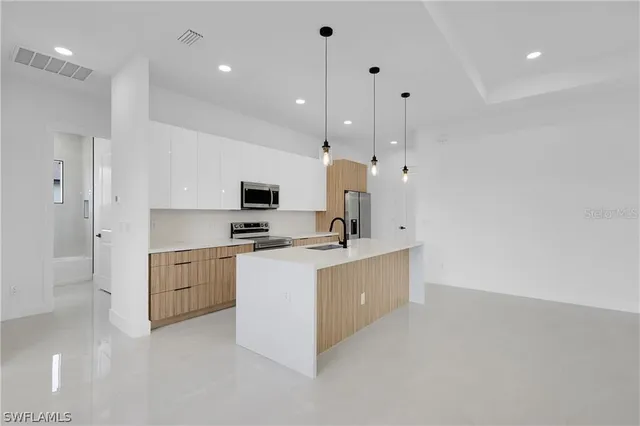 a large white kitchen with stainless steel appliances granite countertop a stove a sink a refrigerator and white cabinets with wooden floor