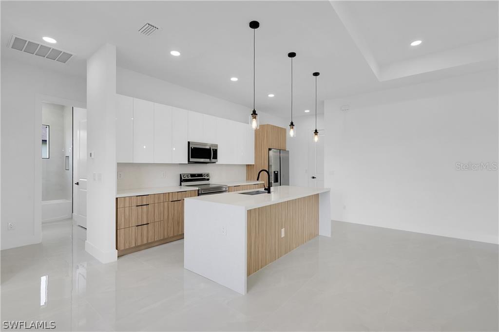 2921 7th Street Southwest Lehigh Acres, FL 33976 - Photo 7 of 8 a large white kitchen with stainless steel appliances granite countertop a stove a sink a refrigerator and white cabinets with wooden floor