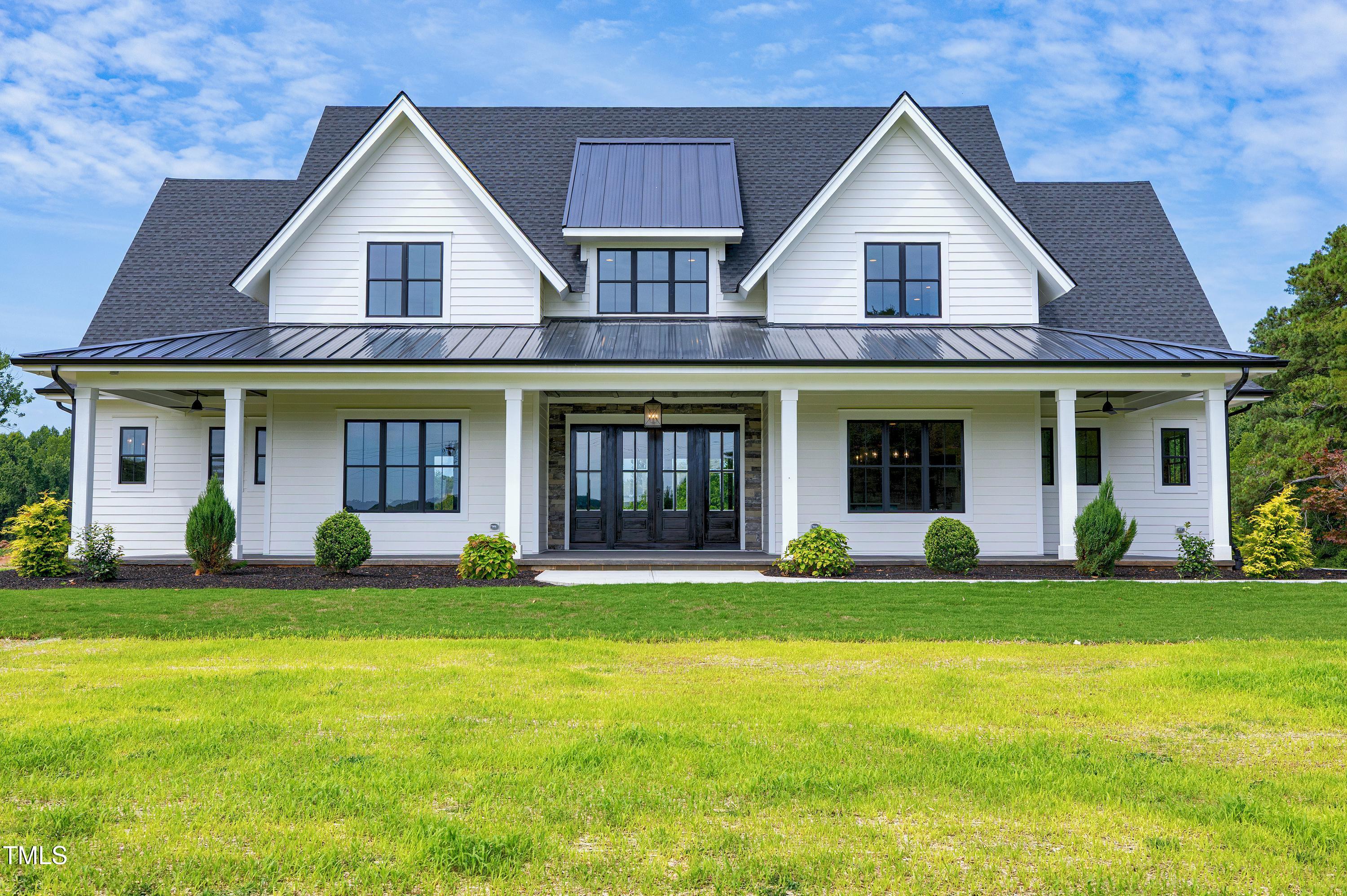 a view of a white house with a large windows and a yard with plants and large trees