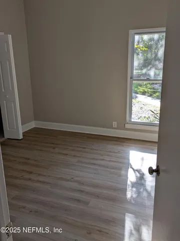 a view of an empty room with wooden floor and a window