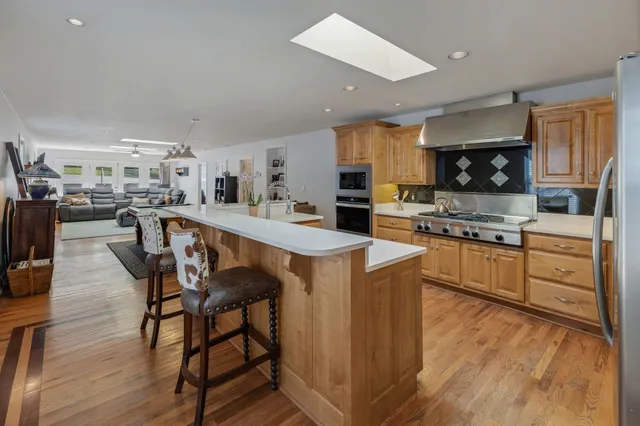 a kitchen with stainless steel appliances kitchen island granite countertop a stove top oven a sink a dining table and chairs with wooden floor