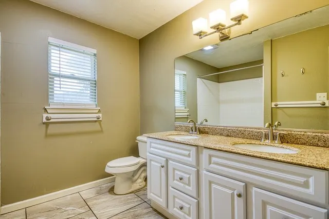 a bathroom with a granite countertop toilet a sink and a mirror