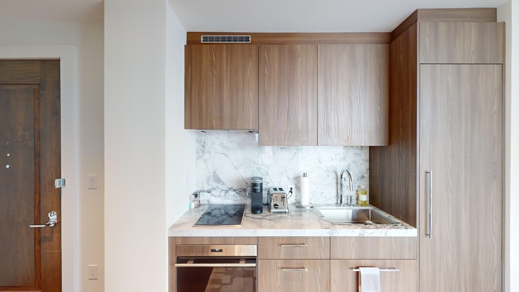 40 Trinity Place, Unit 1605 Boston, MA 02116 - Photo 6 of 16 a kitchen with stainless steel appliances granite countertop a sink a stove and a refrigerator with wooden cabinets