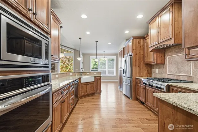 a kitchen with stainless steel appliances granite countertop a stove top oven a sink dishwasher a refrigerator and cabinets with wooden floor