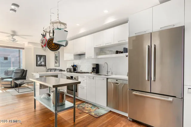 a kitchen with stainless steel appliances a stove a refrigerator a sink dishwasher and white cabinets with wooden floor